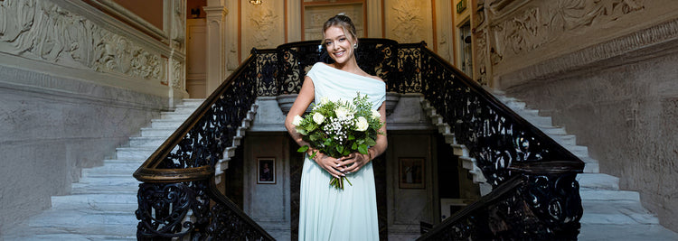 Beautiful woman with a radiant smile, holding a bouquet of roses while wearing a flowing sage green chiffon maxi dress, exuding elegance and grace.