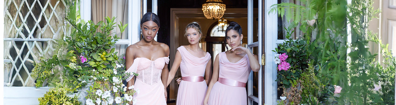 Three women elegantly posing in three different styles of pink dresses, surrounded by a breathtaking backdrop of lush, blooming flower plants. Their unique designs and graceful presence create a dreamy and romantic scene, perfect for wedding